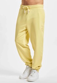 Helle gelbe Sweatpants mit elastischem Bund und Kordelzug. Verfügt über Seitentaschen und ein dezentes gedrucktes Logo am Unterschenkel.