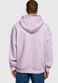 Př oversized světle fialová mikina s kapucí na šňůrku, žebrovanými manžetami a uvolněným střihem, spolu s modrými džíny.
