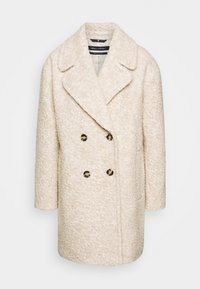 Kræmfarvet, dobbeltbrystet teddyfrakke med fire mørke knapper og brede slag, der har et tekstureret, blødt stof.