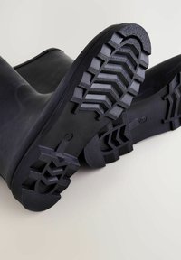 Zwarte rubberen laarzen met een gestructureerde, patroonbodem. De zolen hebben diepe groeven en profielen voor grip en stabiliteit.