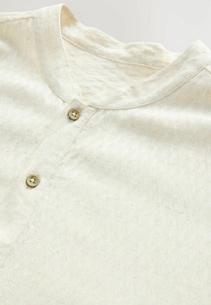 Cream-colored shirt with a textured finish, featuring a round neckline and two small button closures at the front.