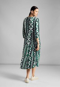 Grünes und weißes, gemustertes Kleid mit Dreiviertelärmeln, gestuften Design und rundem Ausschnitt, kombiniert mit beigen Sneakers.