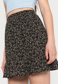 Saia preta floral com cintura elástica, apresentando pequenos padrões roxos e verdes, bainha com frufru e tecido leve.