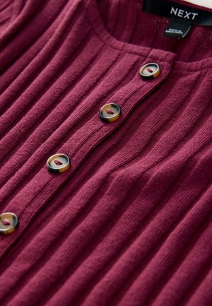 Mørkerød ribstrikket cardigan med fem knapper, med kontrasterende sorte og cremefarvede detaljer omkring knapperne, tekstureret strikket stof.