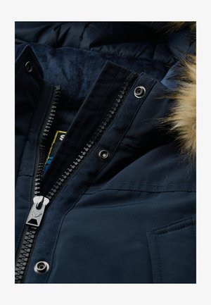 Navy blauwe winterjack met een met nepbont afgewerkte capuchon, contrasterende gladde en gestructureerde stoffen, voorzien van een rits aan de voorkant en drukknopen.