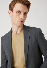 Gray blazer made of a textured fabric, single-breasted with notch lapels, paired with a beige crew-neck t-shirt underneath.
