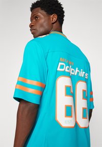 Τυρκουάζ φανέλα Miami Dolphins με πορτοκαλί ρίγες στα μανίκια, το κείμενο "Dolphins" και τον αριθμό "66" σε λευκό πίσω.