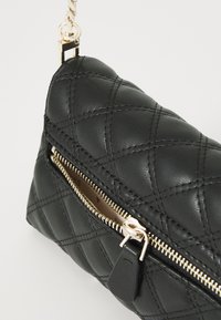 Borsa a tracolla nera in pelle trapuntata con zip dorata, caratterizzata da una finitura testurizzata e una tracolla a catena removibile. Design compatto e slanciato.