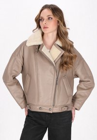 Giacca in pelle marrone con colletto in pelliccia, sagomata con una vestibilità rilassata, dotata di tasche laterali e una cintura in vita per la regolazione.