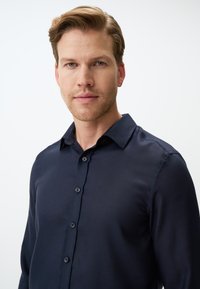 Donkerblauwe langermige shirt gemaakt van een gladde stof, met een button-down kraag en een knoopsluiting aan de voorkant, met een subtiel gestructureerd oppervlak.