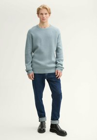 Jasnoniebieski sweter dzianinowy o fakturowanym wzorze, z okrągłym dekoltem i długimi rękawami, zestawiony z ciemnoniebieskimi dżinsami z podwiniętymi mankietami oraz czarnymi botkami za kostkę.