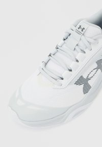 Λευκό αθλητικό παπούτσι Under Armour με ανοιχτό γκρι κορδόνια, πλεκτό επάνω μέρος και ριγέ λογότυπο στο πλάι, σε θέα από μπροστινή γωνία από ψηλά.
