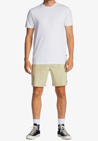 T-shirt en coton blanc associé à un short beige clair. Le modèle porte des baskets montantes noires et des chaussettes blanches. Design simple et décontracté.