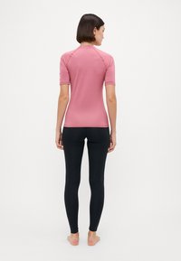 Pielāgota rozā īsām piedurknēm topiņa ar raglan šuvēm un melniem legginsiem, abi izgatavoti no stiept auduma, parādot gludu tekstūru un minimālām šuvēm.