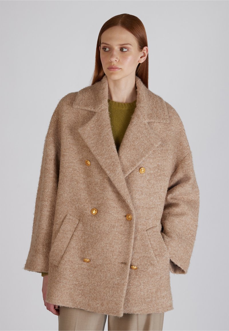 Beżowy płaszcz z wełny z podwójnym zapięciem i klapami, z dużymi złotymi guzikami i kieszeniami naszytymi. Miękka, teksturowana powierzchnia, luźny krój.