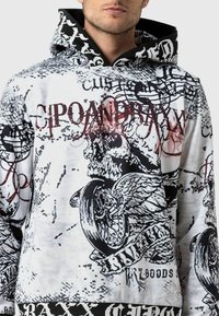 Sweat à capuche avec un design graphique en noir et blanc comprenant des têtes de mort, des ailes et du texte ; fabriqué en tissu doux avec une coupe décontractée.