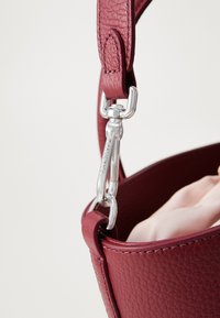 Dark pink textured leather handbag strap attached to bag with a silver clasp engraved with a brand name.