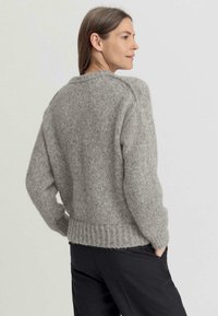 Suéter gris de punto con un corte holgado, dobladillo acanalado y fibras texturizadas. Presenta un escote redondeado y hombros caídos.