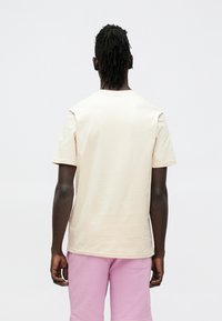 Kortærmet t-shirt i cremefarve med afslappet pasform, glat tekstur og minimalistisk design. Båret med lyserøde shorts.