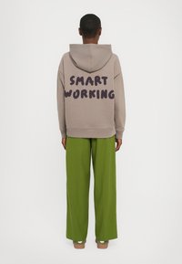 Haut à capuche beige avec "SMART WORKING" imprimé en violet foncé au dos ; associé à un pantalon large vert fluo. Tissu décontracté et doux.