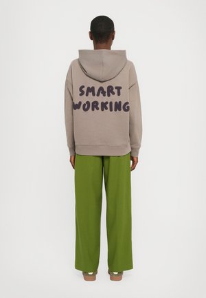 Beige hettegenser med "SMART WORKING" trykt i mørk lilla på baksiden; kombinert med løse, lysegrønne bukser. Uformell, myk stoff.