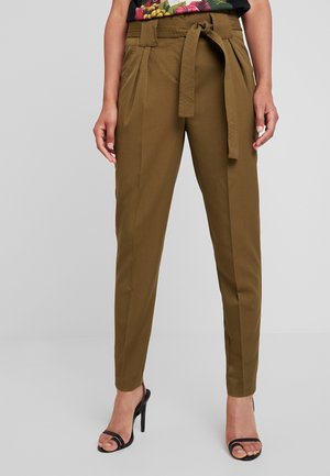 Pantalon fuselé taille haute vert olive avec ceinture en tissu nouée en nœud, porté avec des sandales noires à talons hauts ouvertes à l'avant.