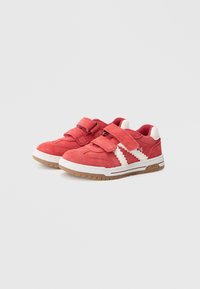 Red suede sneakers with two adjustable straps, white zigzag accents, and a tan rubber sole. Features a logo on the side.