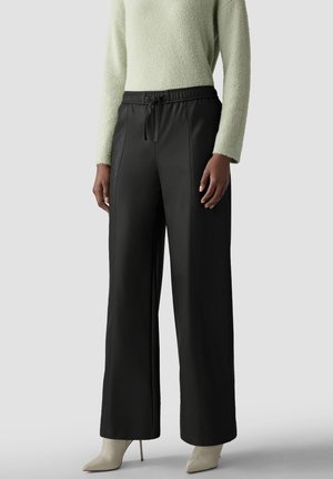 Model wearing black wide-leg pants with drawstring waist, cream textured long-sleeve sweater, and beige pointed-toe high-heeled boots.