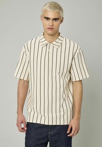 Polo à manches courtes en blanc cassé avec des rayures verticales noires. Doté d'un col classique et d'un tissu texturé. Fermeture à un seul bouton.