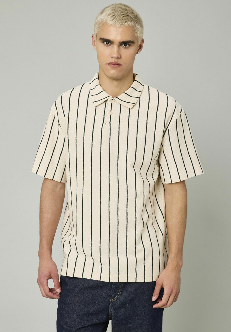 Polo à manches courtes en blanc cassé avec des rayures verticales noires. Doté d'un col classique et d'un tissu texturé. Fermeture à un seul bouton.
