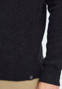 Czarny sweter z dzianiny z prążkowanym dołem i mankietami. Posiada małą metkę z logo w dolnym lewym rogu. Miękka faktura, długie rękawy.