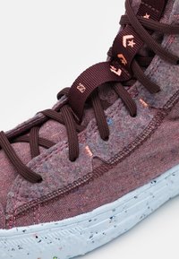 Tyrkysové tenisky z látky s texturovaným svrškem, hnědými tkaničkami a světlomodrou skvrnitou gumovou podrážkou. Výrazné růžové švy a detaily značky.