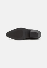 Suela de zapato negra con forma puntiaguda, superficie texturizada y diseño plano. Hecha de goma con ranuras sutiles para tracción.