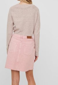 Jupe en denim rose clair avec un ourlet brut, deux poches arrière et un patch en cuir marron à la taille. Pull en maille beige doux centré.