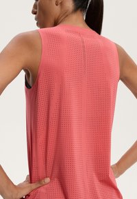 Ujjatlan sportos tank top korall színben, pöttyös mintával és laza fit. Kerek hátsó nyakkivágással és sima textúrával rendelkezik.