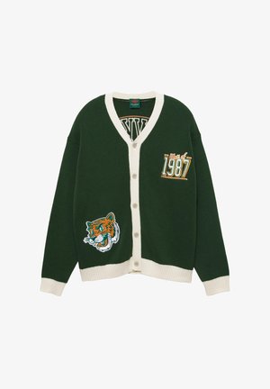 Temnozeleno pulover s gumbi in kremnim robom, z napisom "Razred 1987" na prsih in oznako tigra na spodnjem sprednjem delu.