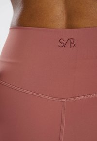 Hoge taille, rekbare leggings in stofroze, met vlakke naden en een geborduurd "S/B" logo op de tailleband. Soepele textuur.
