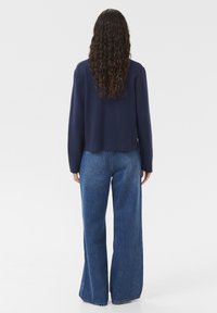 Marinblå kort tröja och vida blå denimjeans. Tröjan har en rund halsringning och långa ärmar; jeansen har en klassisk skärning med lätt fransning.