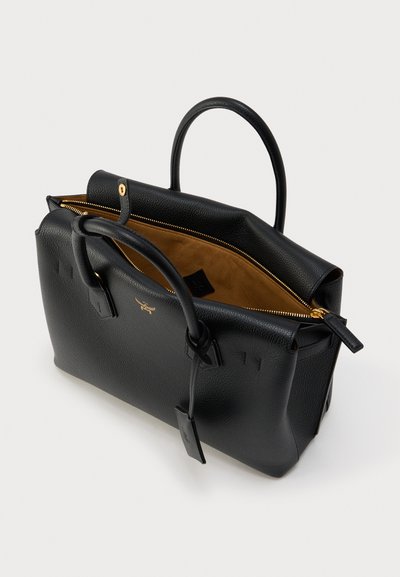 Μαύρη δερμάτινη γυναικεία τσάντα με δύο χερούλια, χρυστό φερμουάρ, ταμπά εσωτερικό και μικρή κρεμαστή ετικέτα, εμφανίζεται μερικώς ανοιχτή σε λευκό φόντο.