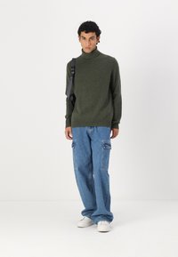 Pull à col roulé vert olive associé à un jean cargo bleu clair à coupe ample et des baskets blanches. Le look présente un design et une texture simples.