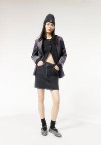 Cárdigan negro corto, minifalda de mezclilla negra, blazer gris, gorro negro y zapatos tipo slip-on con tachuelas, sobre una modelo con cabello largo y lacio.