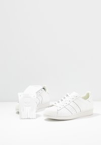 Vita lädersneakers med en klassisk design, som har en skalkappa, grå ränder och en texturerad sula. Inkluderar en vit etikett.