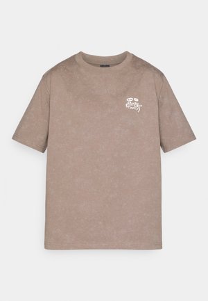 Light brown washed cotton T-shirt with short sleeves and small white graphic logo on the upper left chest reading "Karma" with eyes above.
