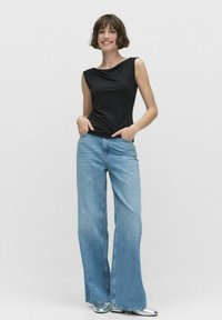 Svart ärmlös topp med draperad halsringning, matchad med ljusblå vida jeans. Outfiten har en avslappnad passform och en mjuk textur.