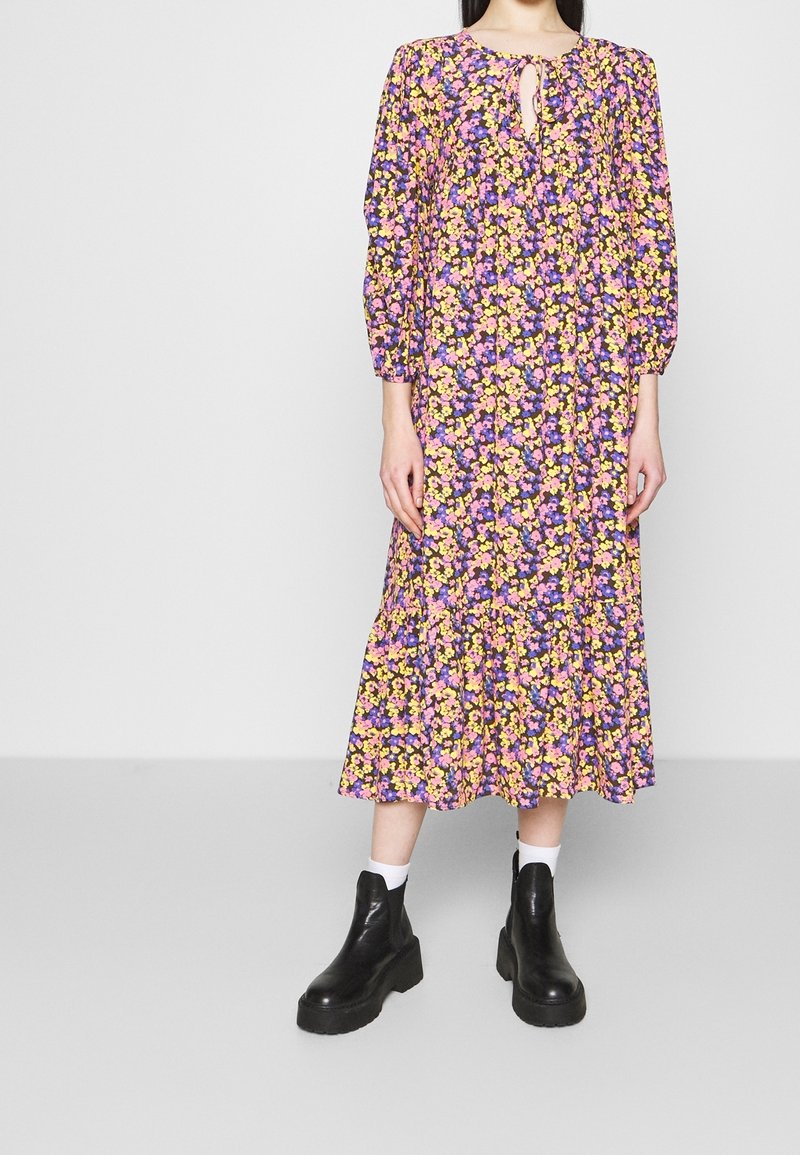 Blommig maxiklänning med långa ärmar, rund halsringning med nyckelhål, främst i lila med gula och rosa blommor; plisserad kjol.