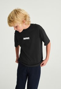 Sort bomulds-T-shirt med korte ærmer, med ordet "FORTNITE" i hvide blokbogstaver centreret på forsiden.