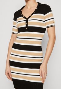Abito lavorato a maglia a righe con strisce alternate di nero, beige e bianco. Maniche corte, scollatura a V con dettagli a bottone dorato.