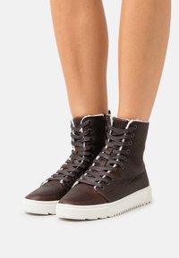 Brown leather high-top sneakers with white rubber soles; feature textured finish, metal eyelets, and fur-lined collar.