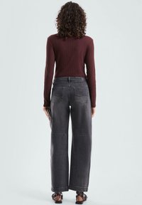 Donkergrijze wijde jeans met een hoge taille, voorzien van achterkantzakken en een gladde textuur, gecombineerd met een geribbelde bordeauxrode blouse met lange mouwen.