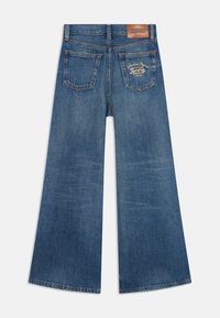 Široke plave traperice s blagim pranjem. Imaju dvije stražnje džepove i kožni mrlju s logotipom na pojasu.